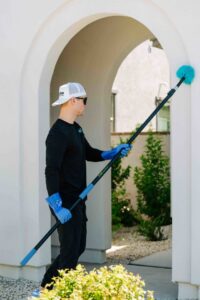 A pest control technician from Aloe Pest Control removing spider webs from a building exterior in Mesa, AZ.