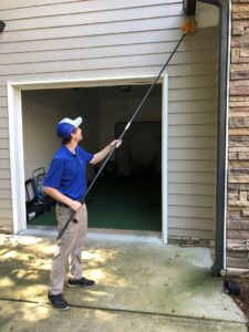 A Capital Pest Services technician removing spider webs or nests from house eaves in Raleigh, NC.