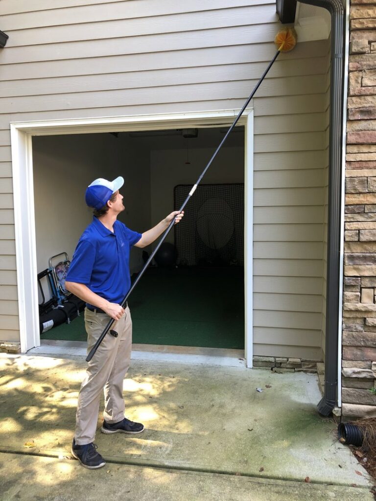 A Capital Pest Services technician removing spider webs or nests from house eaves in Raleigh, NC.