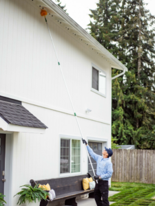 A technician from Insight Pest Solutions- Northwest removing spider webs from the eaves of a house in Federal Way, WA