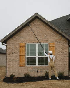A Breezy Pest Control technician removing spiderwebs from the exterior of a house in Little Rock, AR.