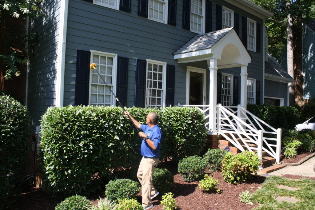 A Capital Pest Services technician removing spider webs or nests from a house exterior in Raleigh, NC.