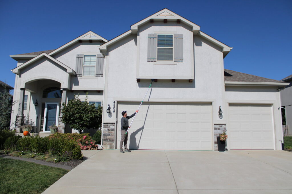 An Upfront Pest technician removing spiderwebs from the exterior of a large house in North Kansas City, MO.