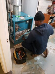 A technician from Booker Heating & Air repairing a boiler or furnace in a basement in Richmond, VA.