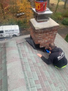 A technician from Elite Home Solutions repairing chimney flashing on a roof, ensuring a secure seal in Warwick, RI.