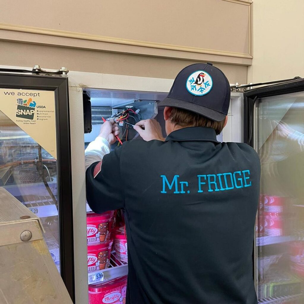 A Mr. Fridge technician repairing a commercial display freezer in Seattle, WA.
