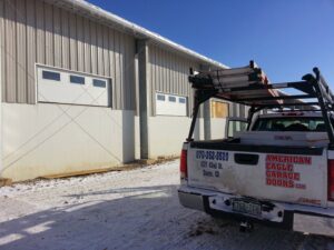 A technician from American Eagle Garage Doors on a ladder repairing a commercial garage door inside a building in Greeley, CO.