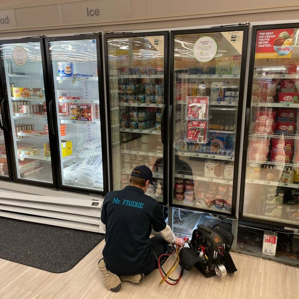 A Mr. Fridge technician repairing a commercial refrigerator in a grocery store in Seattle, WA.