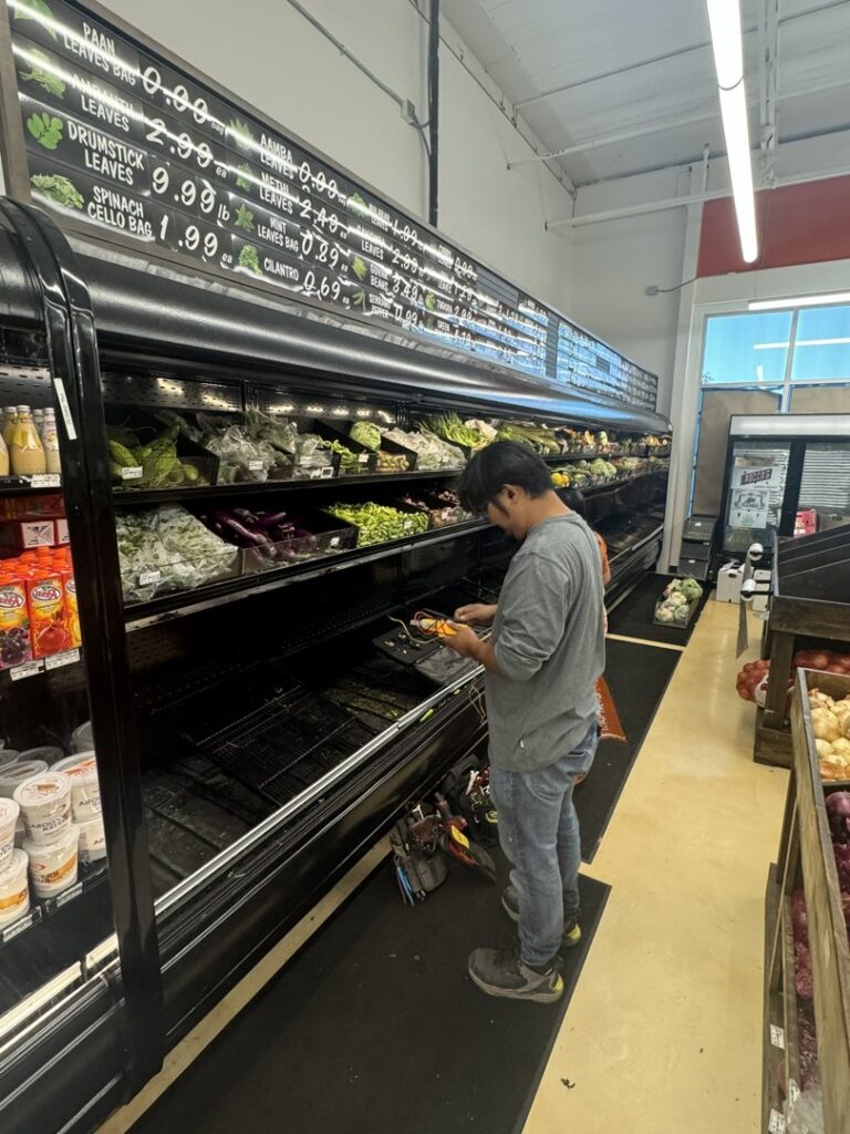 A technician repairing a commercial refrigeration display case in a grocery store for Setpoint Refrigeration LLC in Liberty Hill, TX