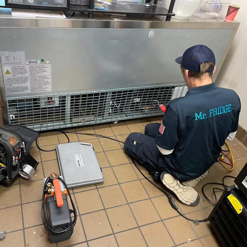 A Mr. Fridge technician repairing the compressor area of a commercial refrigerator unit in Seattle, WA.