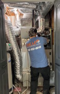 A technician repairing an indoor furnace unit for Ideal Heating & Air Conditioning in Omaha, NE.