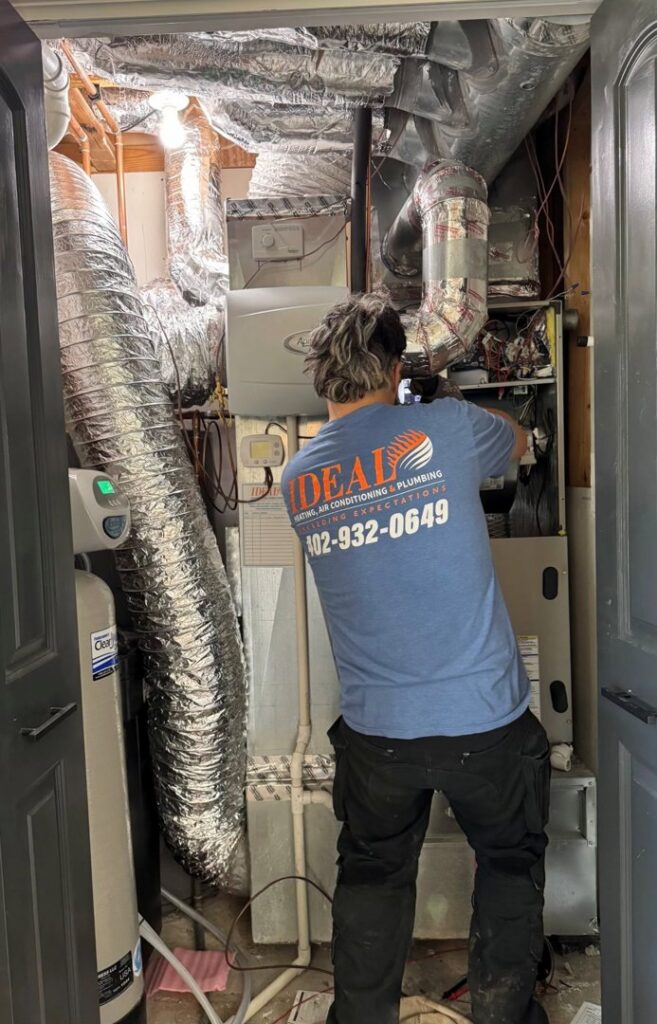 A technician repairing an indoor furnace unit for Ideal Heating & Air Conditioning in Omaha, NE.