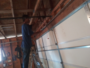 A technician on a ladder repairing a garage door mechanism for Codiwayne Construction & Door in South Bend, IN.