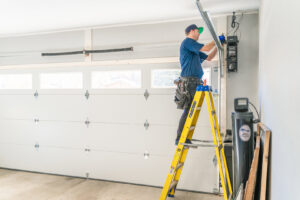 A Blue Fox Garage Doors technician on a ladder repairing a garage door opener system in Gilbert, AZ.