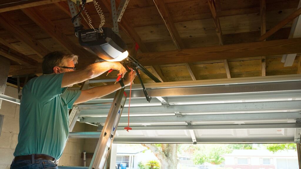 A technician on a ladder repairing a garage door opener and tracks, demonstrating service by Overhead Doors Unlimited, LLC in Appleton, WI.