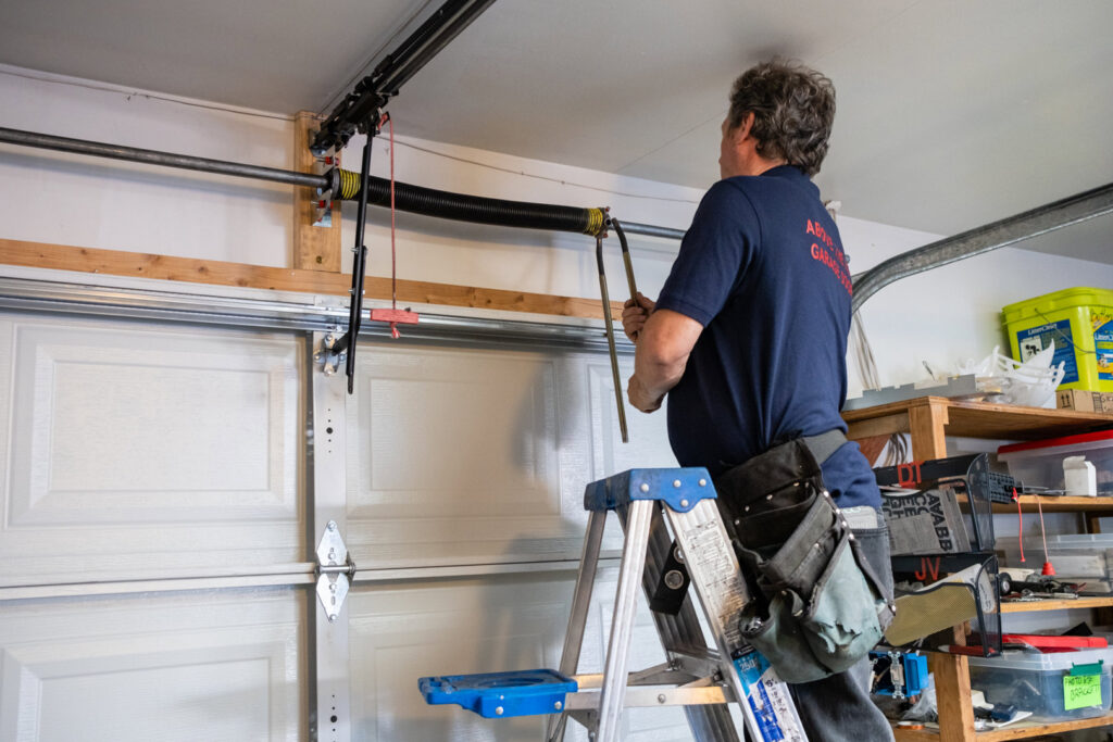 A garage door technician on a ladder repairing or installing a torsion spring system for Above The Rest Garage Door in Colorado Springs, CO.