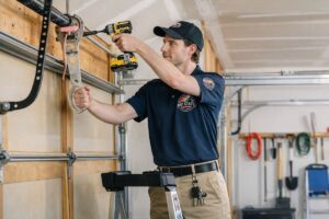 A Baystate Garage Door technician repairing a garage door spring mechanism with a drill in Milton, MA.