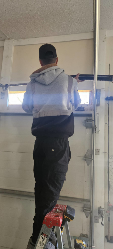 A Skreno Services technician on a ladder repairing a garage door spring in Summerville, SC.