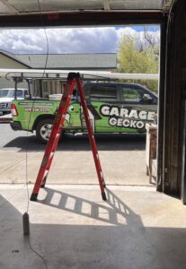 A Garage Gecko technician on a ladder repairing garage door springs and tracks in Spokane, WA.