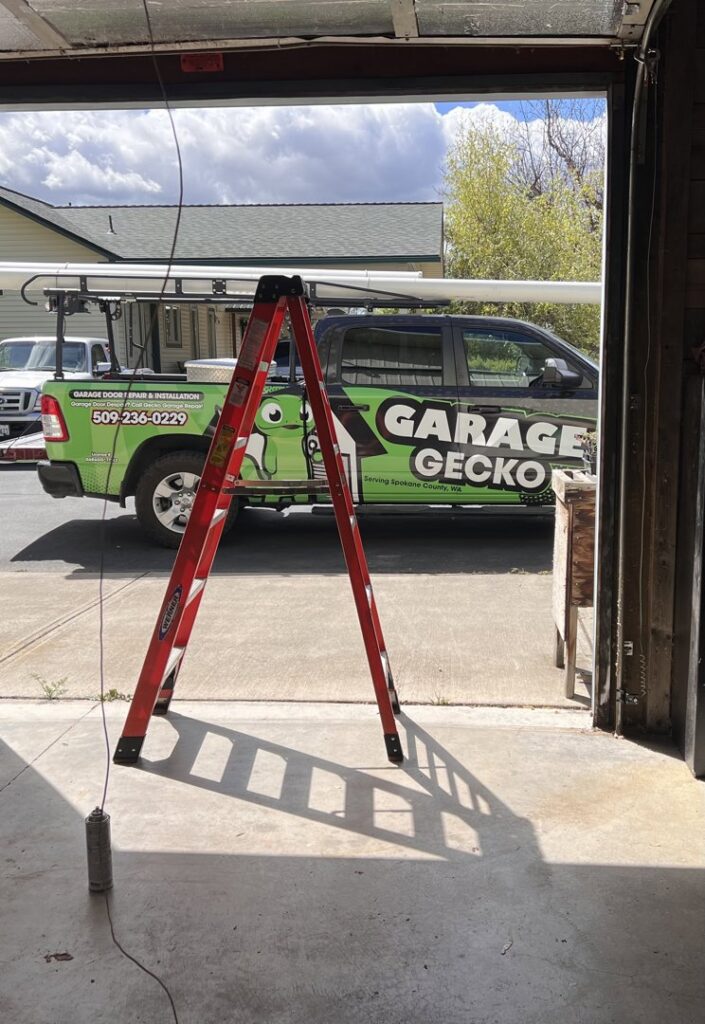 A Garage Gecko technician on a ladder repairing garage door springs and tracks in Spokane, WA.