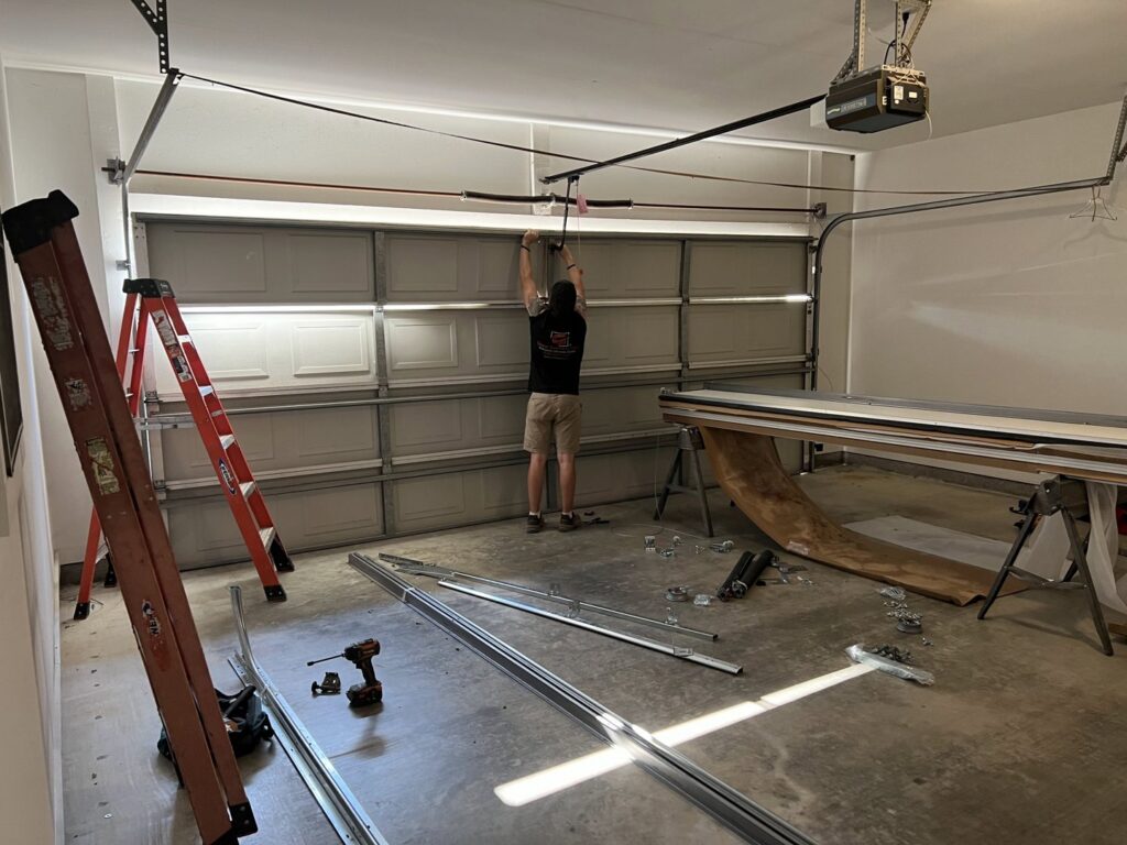 A Geaux Overhead Door technician repairing garage door springs and mechanism inside a residential garage in West Monroe, LA.