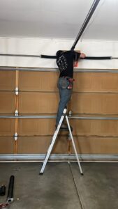 A technician on a ladder repairing or installing garage door springs and torsion bar for Greeley garage door repair in Greeley, CO.