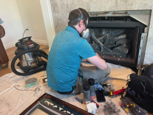 A technician wearing a respirator, performing maintenance or repair on a gas fireplace for Precision Energy LLC in Everett, WA.