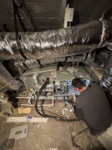A Community Mechanical technician repairing an indoor furnace or air handler unit in Plano, TX.
