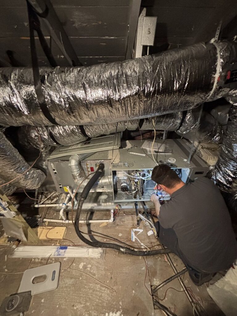 A Community Mechanical technician repairing an indoor furnace or air handler unit in Plano, TX.