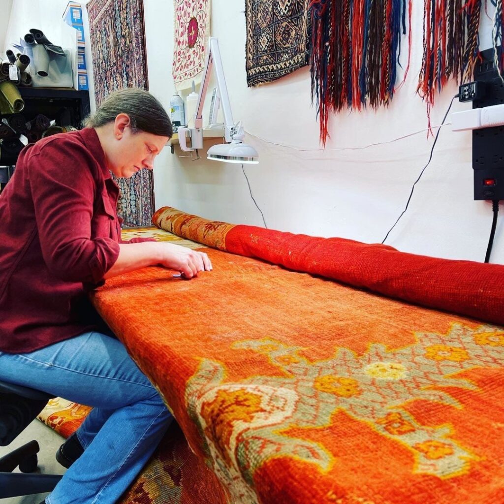 A skilled technician meticulously repairing a large orange rug at Renaissance Rug Cleaning Inc. in Portland, OR.