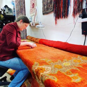 A skilled technician meticulously repairing a large orange rug at Renaissance Rug Cleaning Inc. in Portland, OR.