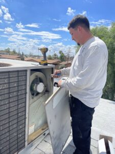 A technician repairing an outdoor HVAC unit, with its panel open, for 365 Mechanical in Mesa, AZ.