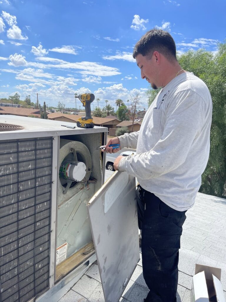A technician repairing an outdoor HVAC unit, with its panel open, for 365 Mechanical in Mesa, AZ.