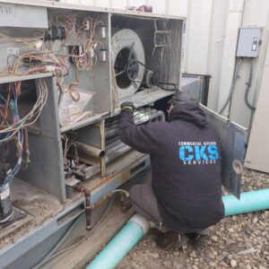 A technician from Commercial Kitchen Services, LLC of Watertown, SD, repairing an outdoor commercial HVAC unit with its panel open.