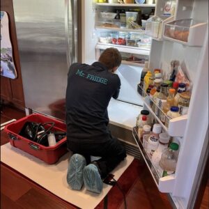 A Mr. Fridge technician kneeling to repair a residential refrigerator freezer in Seattle, WA.