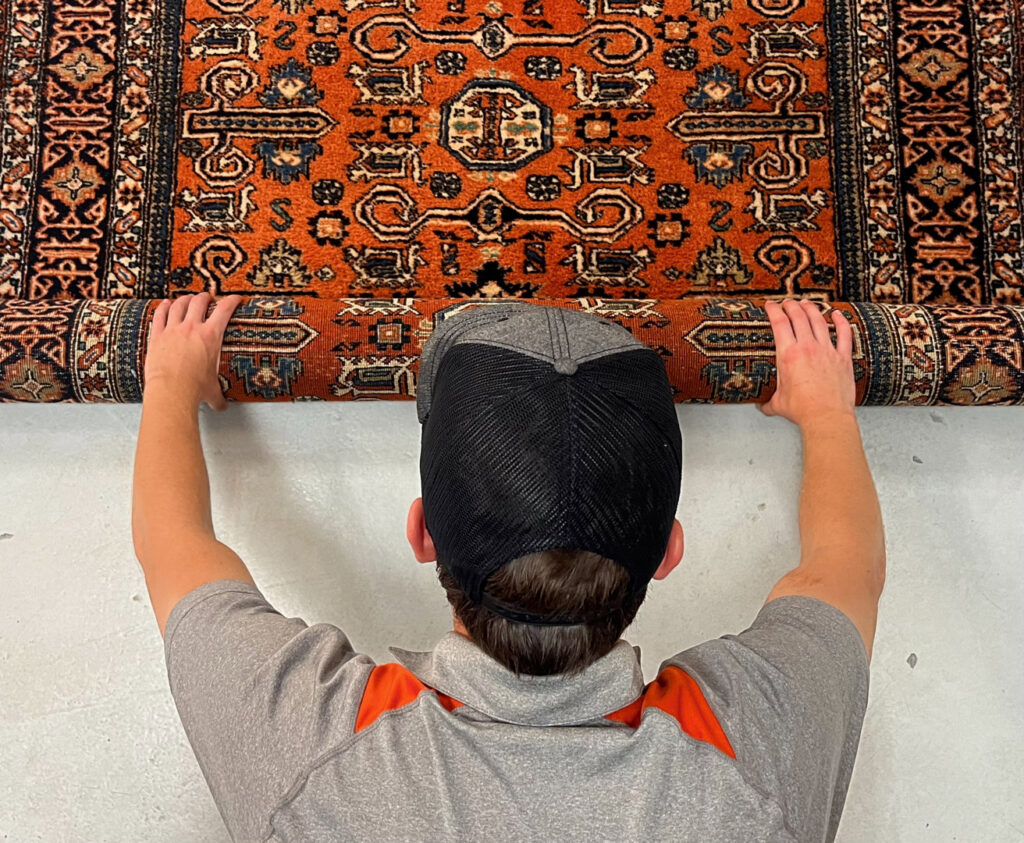 A technician carefully rolling up an ornate area rug, preparing it for cleaning or transport by Carpet & Rug Cleaning in Mount Pleasant, SC.
