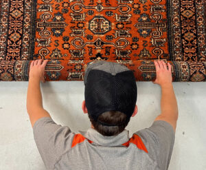 A technician carefully rolling up an ornate area rug, preparing it for cleaning or transport by Carpet & Rug Cleaning in Mount Pleasant, SC.