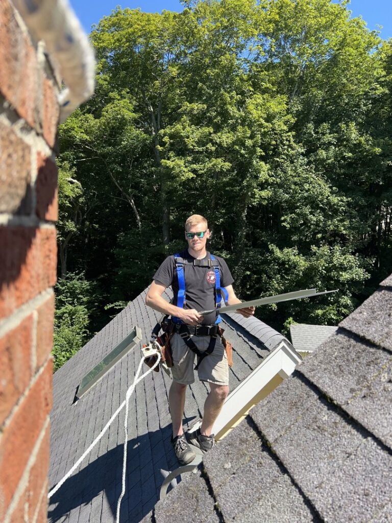 A Defense Pest and Wildlife Control technician on a roof, wearing a safety harness and installing exclusion flashing in Hartford, CT.