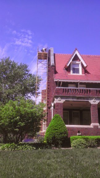 A technician on scaffolding working on a chimney, likely for wildlife exclusion or repair, by Critter Control of Omaha, NE