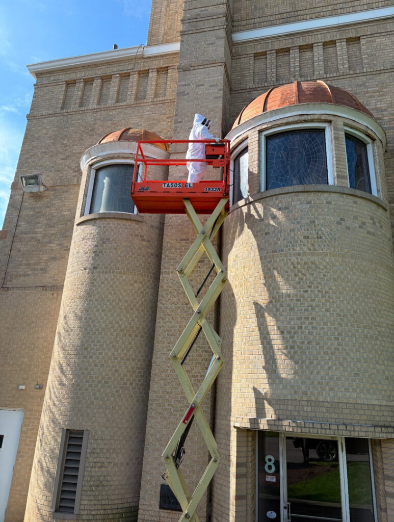 A technician in a bee suit on a scissor lift performing high-reach pest control for Antix Pest Control in Canton, OH.