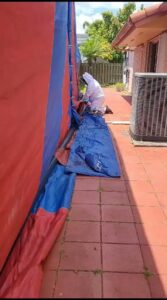 A technician in a protective suit securing a fumigation tent around a house for Monster Pest Control in Miami, FL.