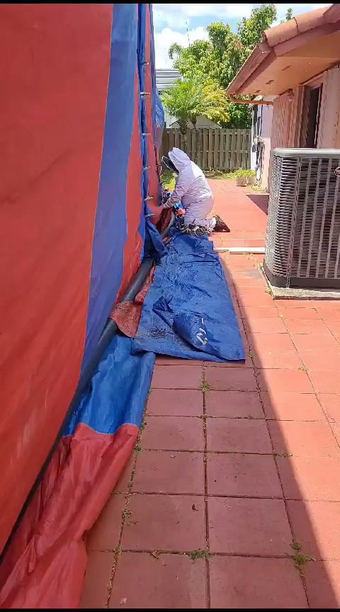 A technician in a protective suit securing a fumigation tent around a house for Monster Pest Control in Miami, FL.