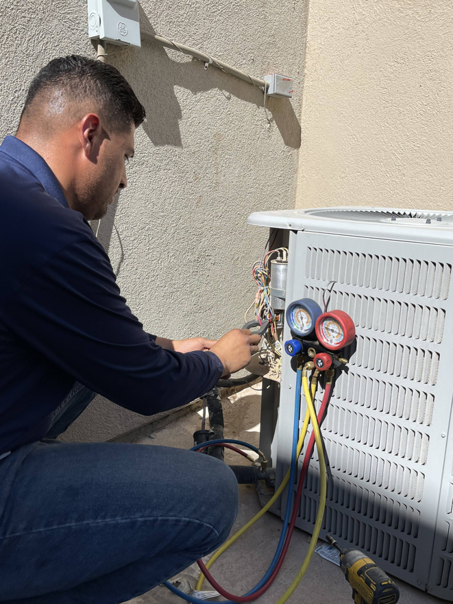 A technician servicing an outdoor AC condenser unit with gauges for Lone Star Mechanical in El Paso, TX.