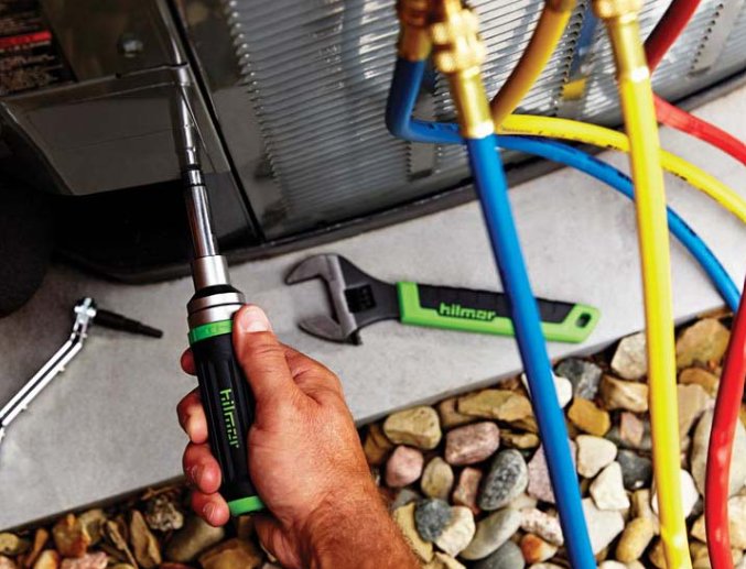 A technician servicing an outdoor AC unit with refrigerant lines visible, performed by The Right Flow Heating and Air LLC in Lawton, OK