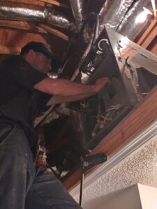 A technician from TJ Mechanical Services LLC servicing an air handler unit in an attic or crawl space in Rock Hill, SC.