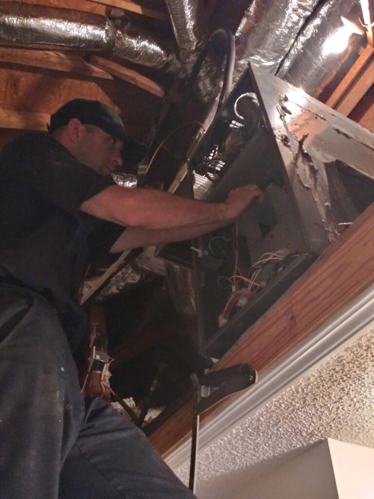 A technician from TJ Mechanical Services LLC servicing an air handler unit in an attic or crawl space in Rock Hill, SC.