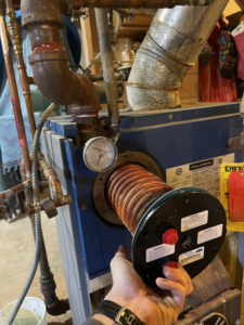 A technician's hand servicing a heat exchanger coil in a boiler unit, demonstrating work by Force Mechanical Services in Churchville, MD.