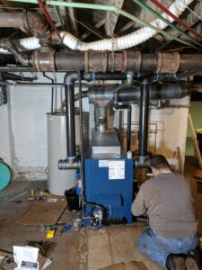 A Huether Heating & Cooling Inc technician servicing a large blue boiler system in a Rochester, NY basement.