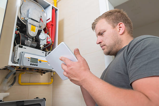 A technician servicing an open boiler unit while using a tablet for diagnostics at Infinity Heating & Cooling by Rivera in Kenosha, WI.