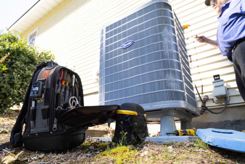 An R&R Heating & Air Conditioning technician servicing an outdoor Carrier AC unit with tools in Spokane, WA.